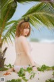 A woman in a bikini sitting under a palm tree on the beach.